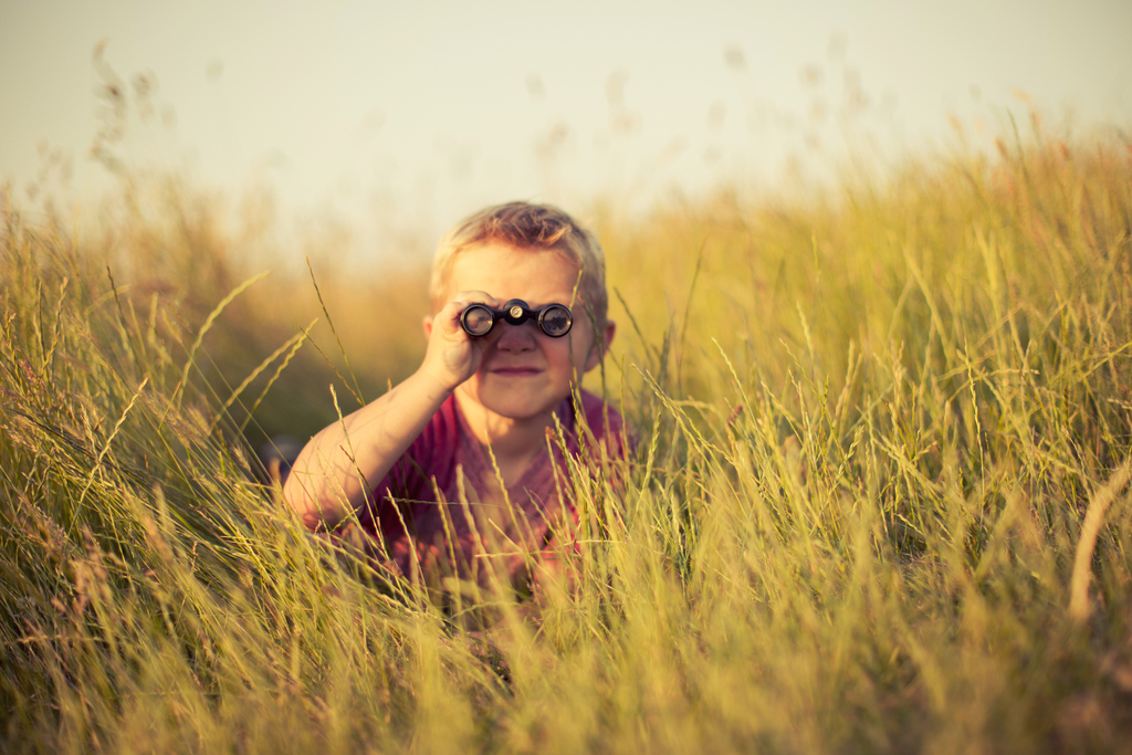 Young Boy Looking Through Binoculars Hiding in Grass