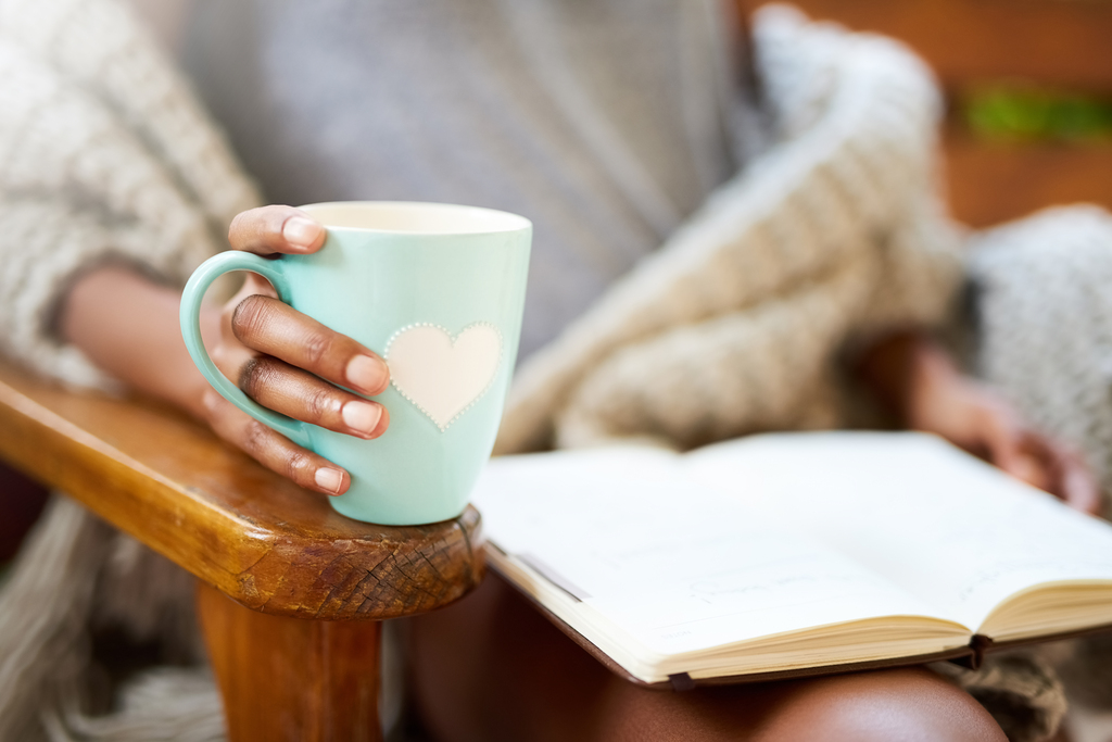 Cropped shot of a woman relaxing with a book and a cup of coffee